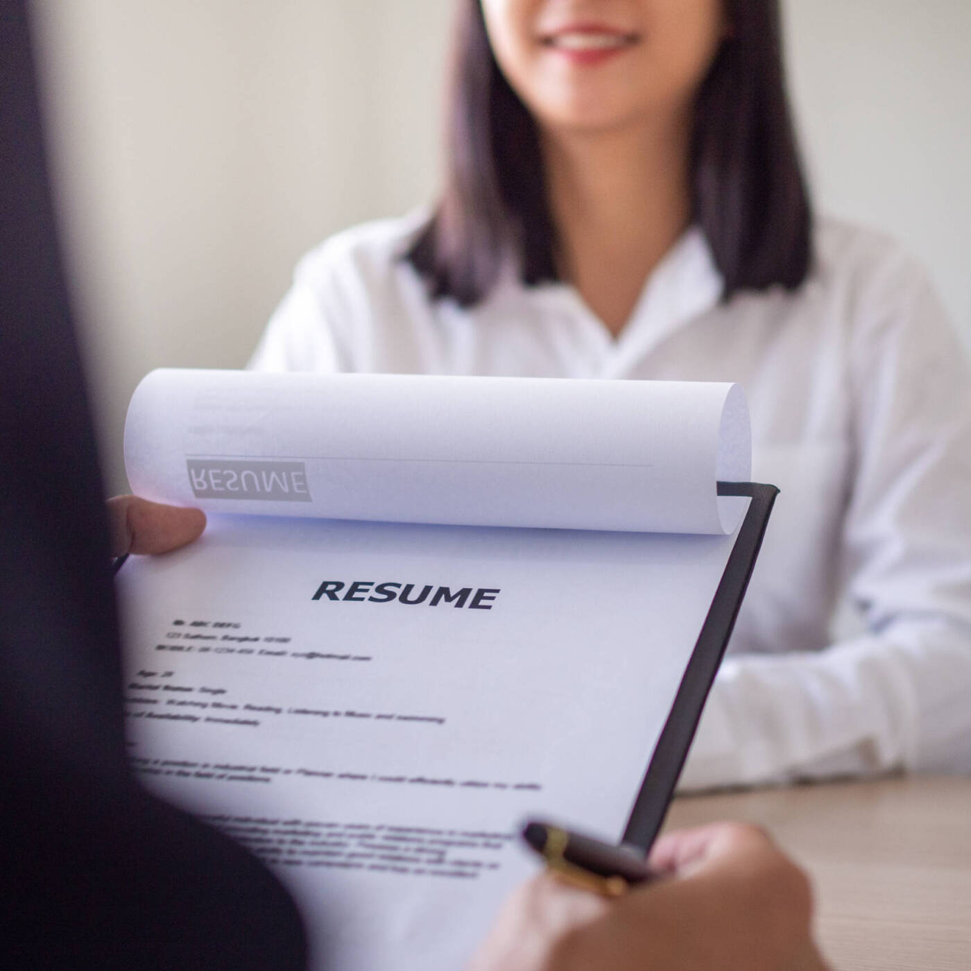 Looking at resume on clipboard with applicant in distance